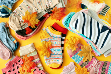 Colorful socks and maple leaves. A lot of socks on a yellow background. Multi-colored socks for the cold seasons. Clothing for autumn and winter. Socks of different sizes.