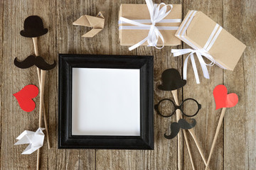 A flat composition of frames, gift boxes, holiday accessories, mustaches, origami birds and hearts on an old wooden background. Template for text, top view.