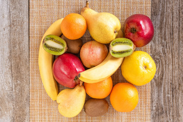 Bananas, apples, kiwis, oranges, lemons, and pears lay in a heap on the wooden surface.