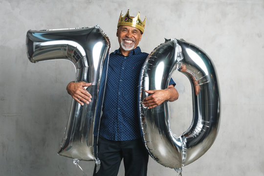 Cheerful senior man holding silver balloons for his 70th birthday celebration - Powered by Adobe