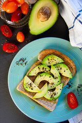 Wholesome brunch idea - avocado on wholemeal toast, sprinkled with black pepper, cherry tomatoes on the side, vegan healthy meal, home cooked and family friendly. Bright colours, contrasty flat lay.