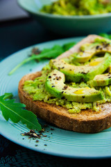 Close up of avocado smash on wholemeal toast with rocket salad and splash of olive oil, sprinkled with black pepper, vegan healthy meal. Shallow depth of field, close up.