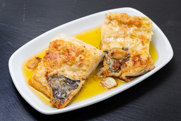fried cofish with garlic and olive oil on white dish on ceramic background