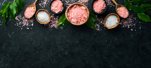 Pink fragrant sea salt in a bowl. On a black stone background. Spa treatments. Top view. Free space...