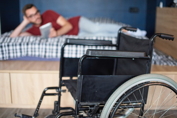 Man reading in bed, wheelchair in front