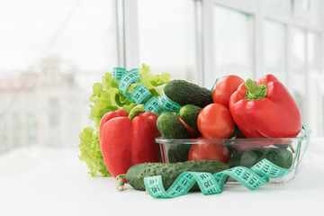 measuring tape lie in big transparent plate with vegetables: salad, tomatoes, bell peper, zucchini,...