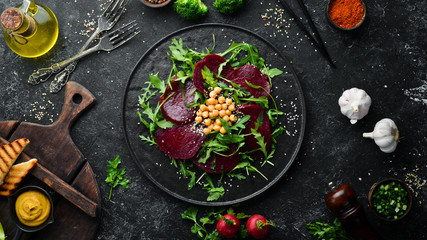 Vegan salad: beets, arugula and chickpeas on a black stone plate. Healthy diet food. Top view. Free space for text.