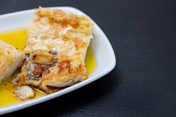 fried cofish with garlic and olive oil on white dish on ceramic background