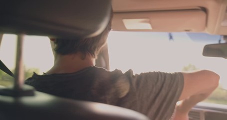 Teenager drives the car while sunset and makes an u-turn.  Rear View to young man drives a car.  Young man driving the car. Teen boy  driving car. Sun's rays shine through the windshield of the car