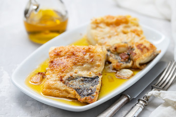 fried cofish with garlic and olive oil on white dish on ceramic background