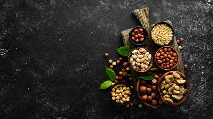 Obraz na płótnie Canvas Assortment of nuts: pistachios, hazelnuts, pine nuts on a black stone background. free space for your text. Top view.