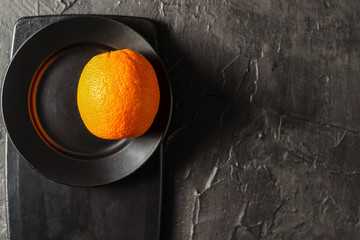 fresh whole orange on a smooth black plate and cutting black Board and on a textured black background