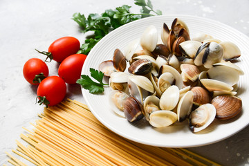 seafood pasta ingredients: clams, spaghetti, tomatoes and parsley. recipe for traditional Italian pasta Spaghetti alle Vongole. on a gray background. top view, food flat lay