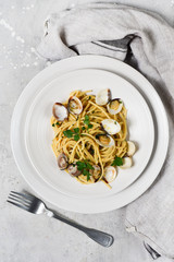 Traditional italian food seafood pasta with clams and parsley Spaghetti alle Vongole in white plates on a grey background. top view
