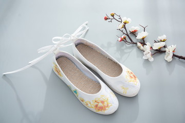 White embroidered shoes with beautiful embroidery and a bouquet of flowers next to them.
