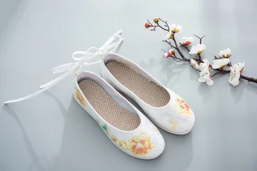  White embroidered shoes with beautiful embroidery and a bouquet of flowers next to them. © InkheartX