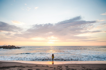 Young millennial female backpacker standing at the edge of the shoreline watching sunset over the Pacific Ocean in Las Peñitas, Nicaragua