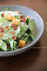 Caesar salad with crispy bread and bacon close up on wood background