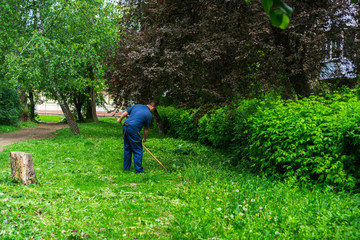 a man with a scythe in a blue uniform mows grass