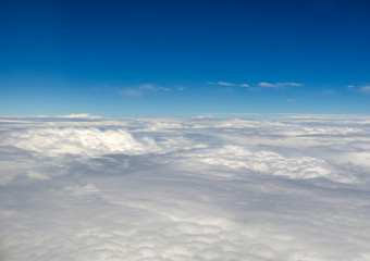 Naklejka na ściany i meble Gorgeous dense clouds and the bright blue horizon of the sky from the height of a flying airplane. Smooth calm landscape of white clouds. Sky background with space for text.