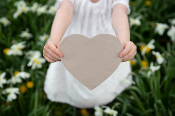 The girl gives a paper heart for Mother's Day, Father's Day, birthday, apology among flowers