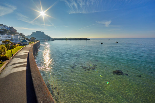 Image of Gorey promenade with Gorey Castle and harbour in the background at high tide with a blue sky and early morning sunshine. Jersey, Channel Islands, Uk