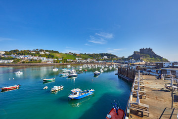 Fototapeta na wymiar Image of Gorey Harbour with fishing and pleasure boats, the pier bullworks and Gorey Castle in the background with blue sky. Jersey, Channel Islands, UK