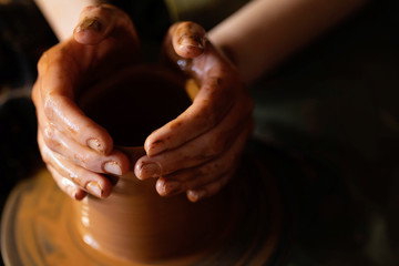 A potter hands moulding a clay pot on rotating potter's wheel.