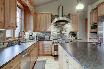 Large luxury wooden kitchen interior with light wood hardwood floor and dark granite slab on island...