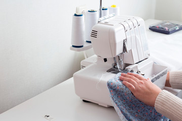Selective focus. in the atelier of a sewing workshop, a young girl sews a dress on an overlock. hands hold the fabric and stitch the details. place for inscription