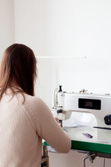in the atelier of a sewing workshop, a young girl sews a dress on an overlock. hands hold the...