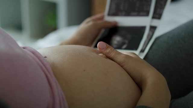 Video of pregnant woman stroking abdomen and browsing ultrasound images. Shot with RED helium camera in 8K 