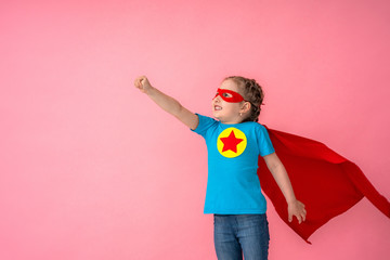 beautiful little girl in superhero costume in red Cape and mask shows how strong