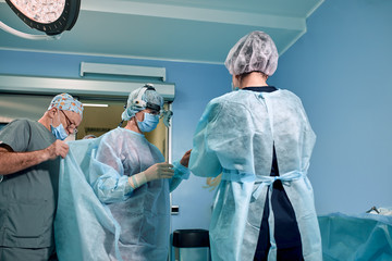 A team of surgeons is preparing for surgery. Surgeons wear sterile clothing before surgery with the help of nurses, sterile gowns, gloves, masks, in the intensive care unit.