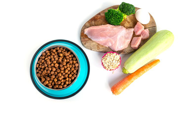 Foreground bowl with dry food for animals and various ingredients of healthy food in the background. Dog food concept. Top view