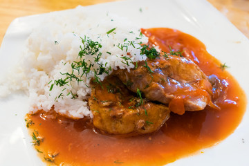 Fried pork in a sauce with rice and herbs on a plate