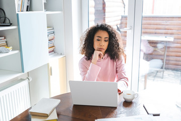 african american freelancer looking at laptop near smartphone, books and cup