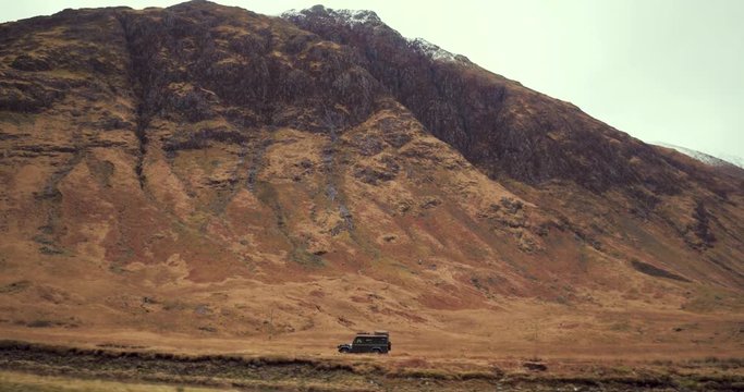 Scale of car driving through valley given by huge mountain behind. Low tracking shot