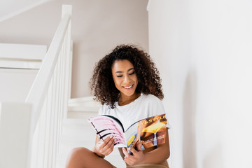 happy african american woman sitting on stairs with magazine