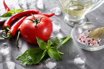 red chili peppers, green Basil sprigs,  fresh red tomato,  spices, salt, oil, ice cubes on a gray