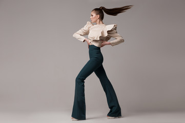 Fashionable look, a woman in long green flared trousers, a silk beige blouse with wide magnificent sleeves. A model poses in a studio on a light background, her hair is flying. Fashion clothes. - 351602678