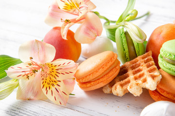 Obraz na płótnie Canvas peach, green macaroon cookies with yellow Alstroemeria flowers, apricots, waffle on a beige background