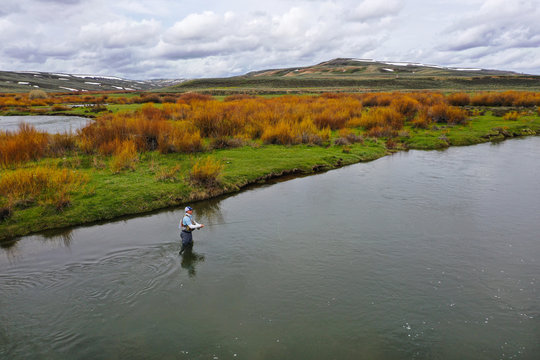 an aerial shot of a man fly fishing on a river.