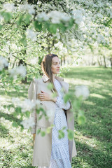 Beautiful young girl walks in the park, flowering trees, spring, sunny weather. Girl in a white dress. Blooming trees, beautiful nature, summer. Style, freedom, clothes