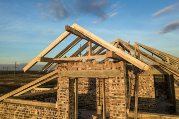 Private residential house with wooden roof frame structure under construction. Unfinished brick building under development.