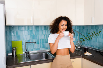 happy african american girl looking at camera and holding cup of coffee
