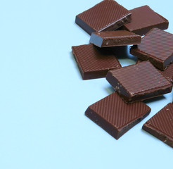 a bar of dark chocolate is broken into pieces, lies on a blue background. Place for text,...