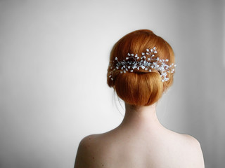 Young red-hair girl with a volume and sleek low hair bun, decorated with headpiece, back view, hairstyling concept