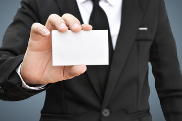 Businessman showing white piece of paper in black suit. Idea for business credit card or visiting card.
