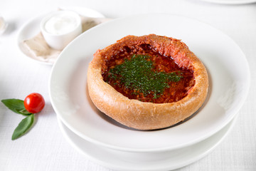 Russian traditional borsch in the bread with rye dark bread, spices and herbs on a light background